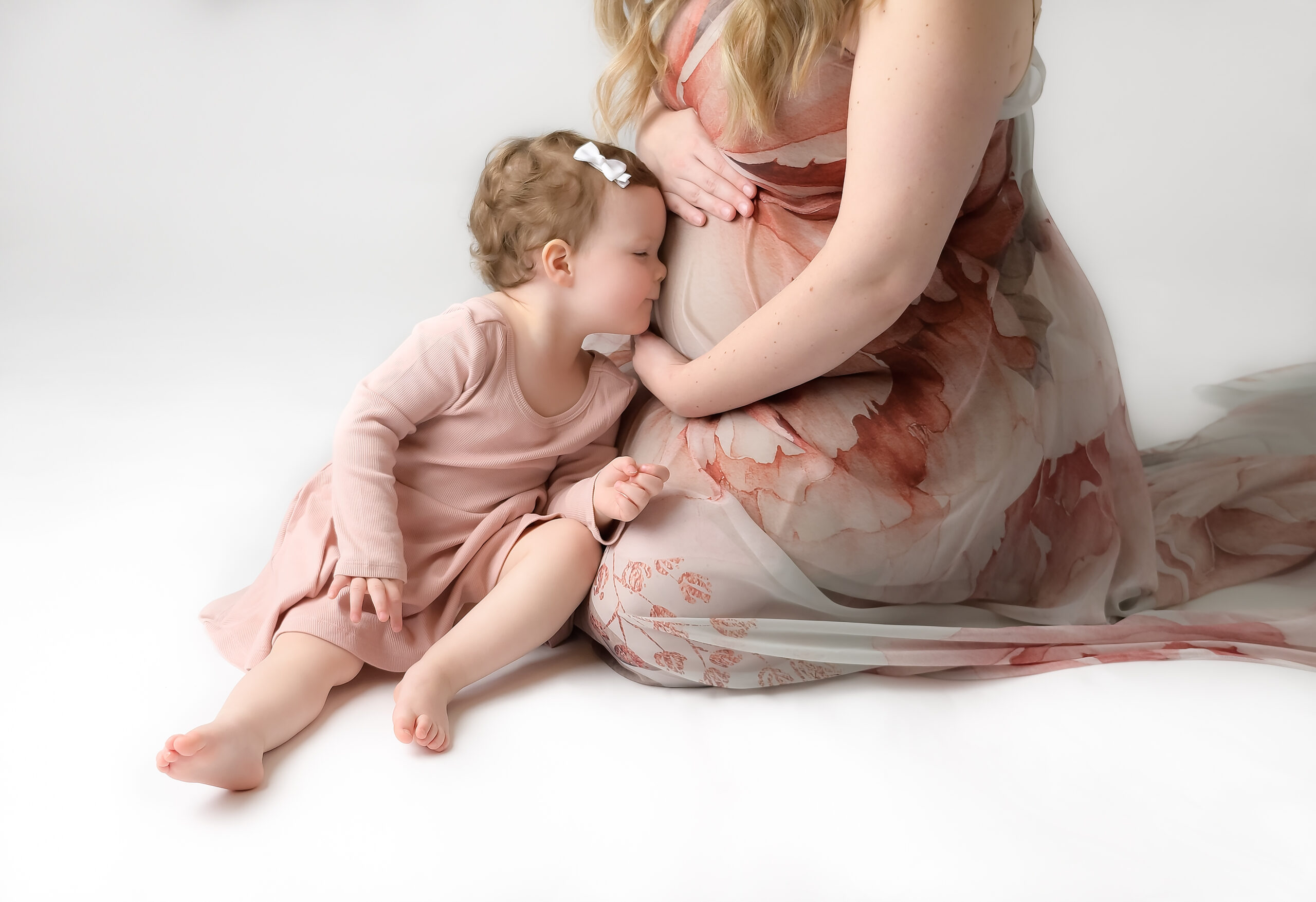 Big sister to be kisses mommy's tummy during a family maternity photo session