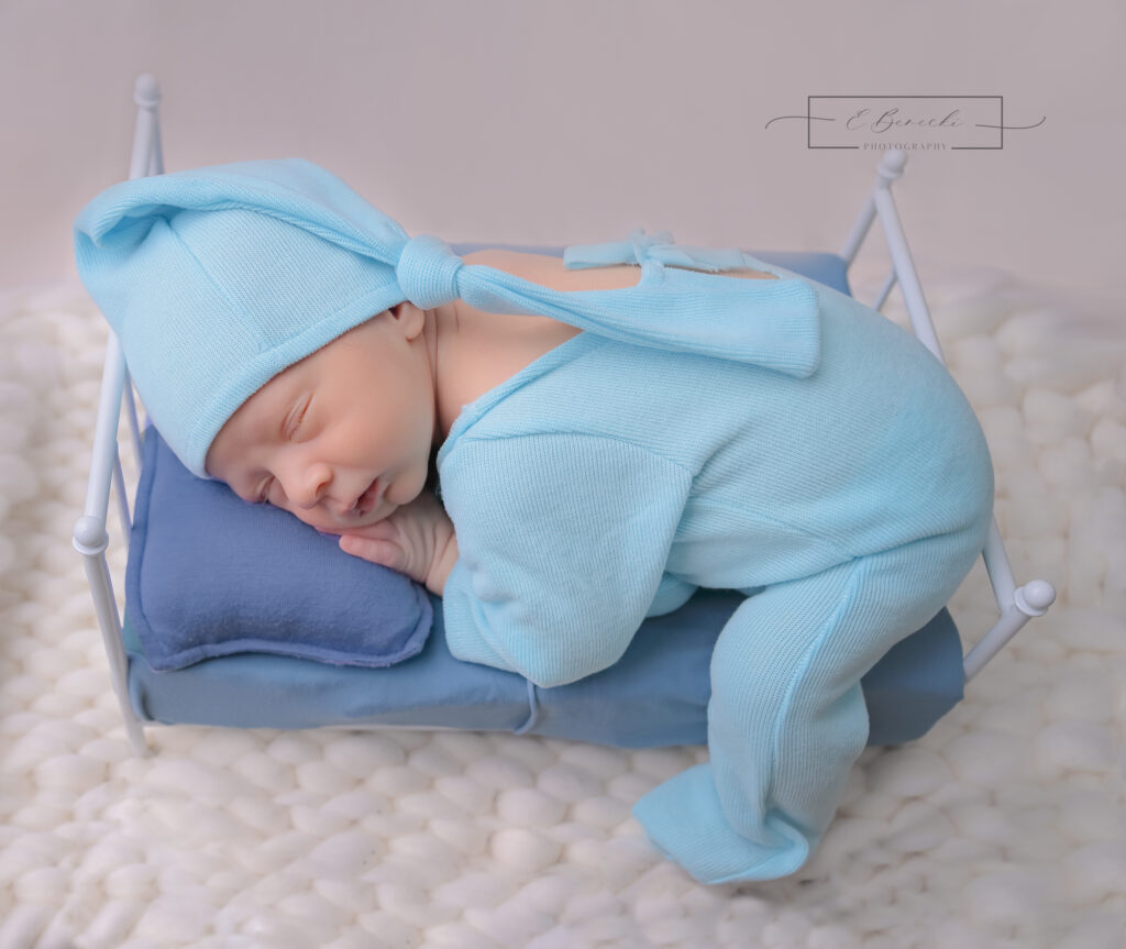 Baby boy in blue sleeping on a tiny bed prop during his newborn photography session near Gig Harbor.