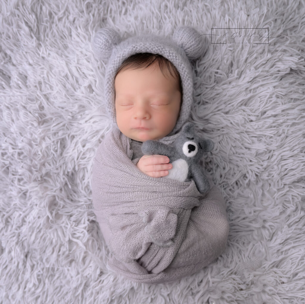 Newborn baby wrapped in soft grays snuggling with a bear during a newborn photo session near Gig Harbor.