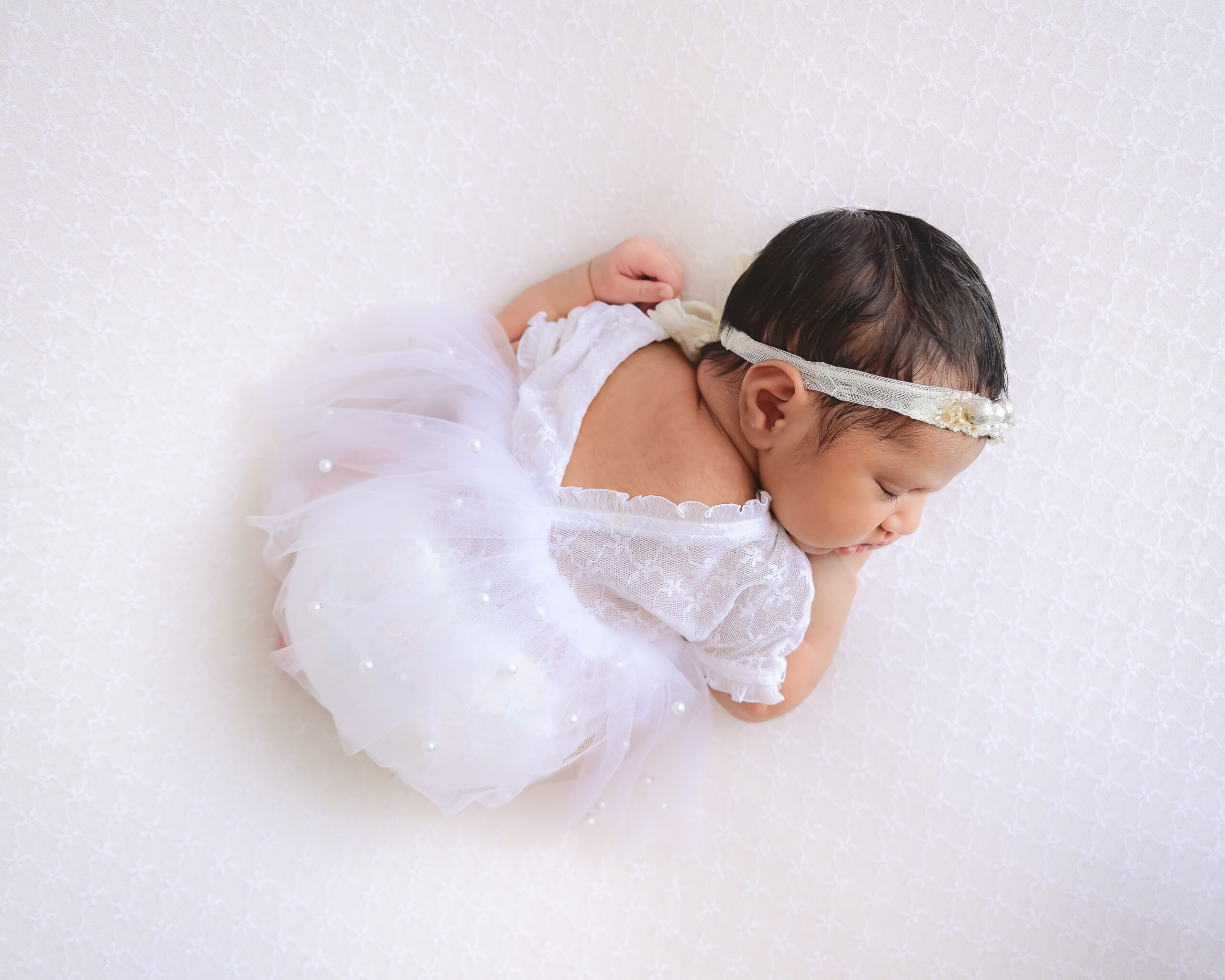 Newborn girl sleeping on belly in white dress on white background