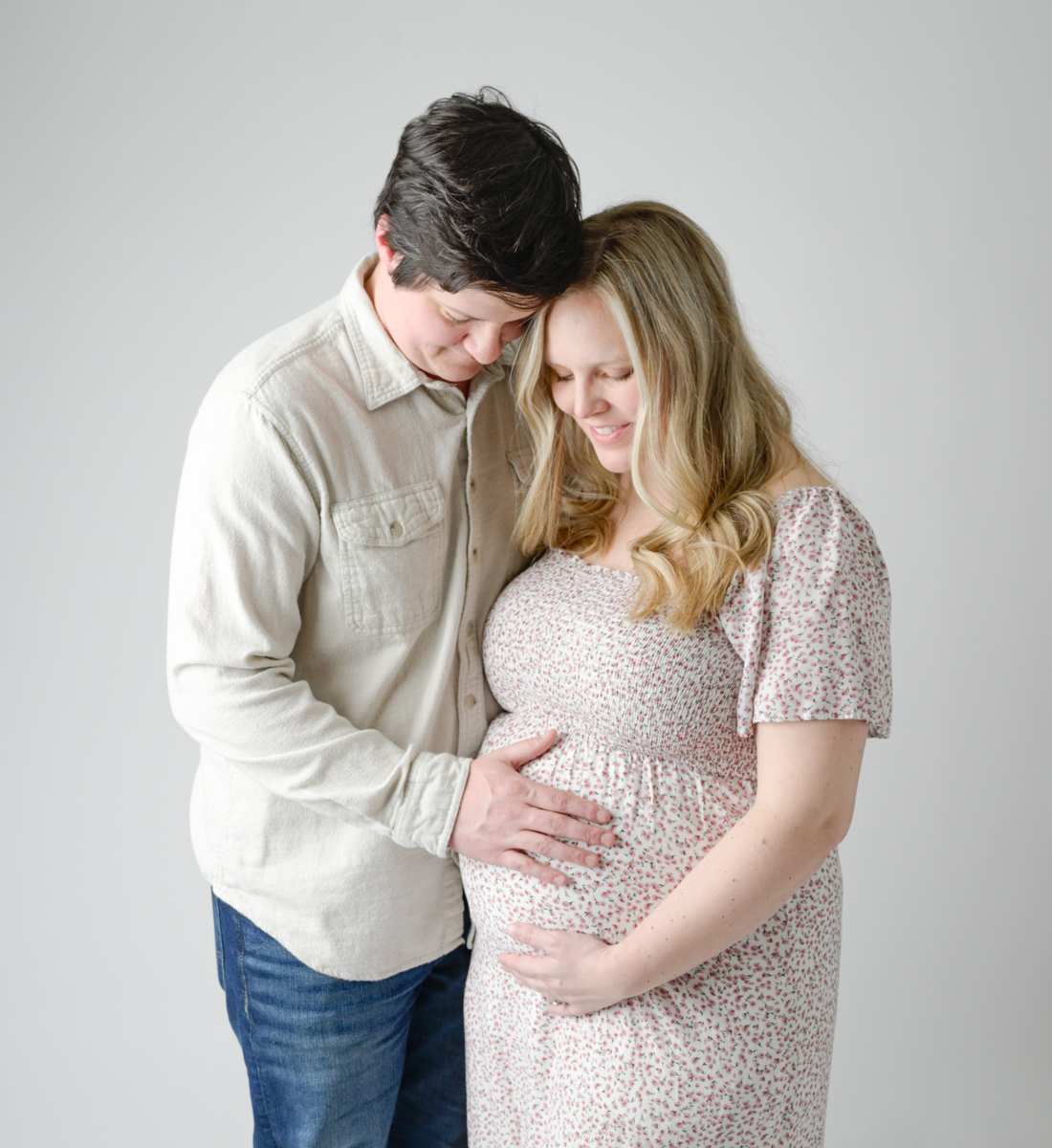 Husband and mom to be looking at her baby bump set against a light background.