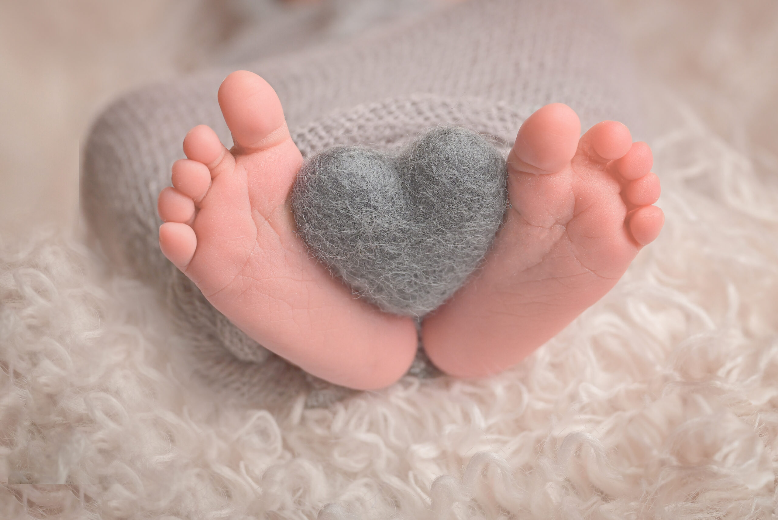 Newborn photo session with a gray heart placed and held by newborn's feet