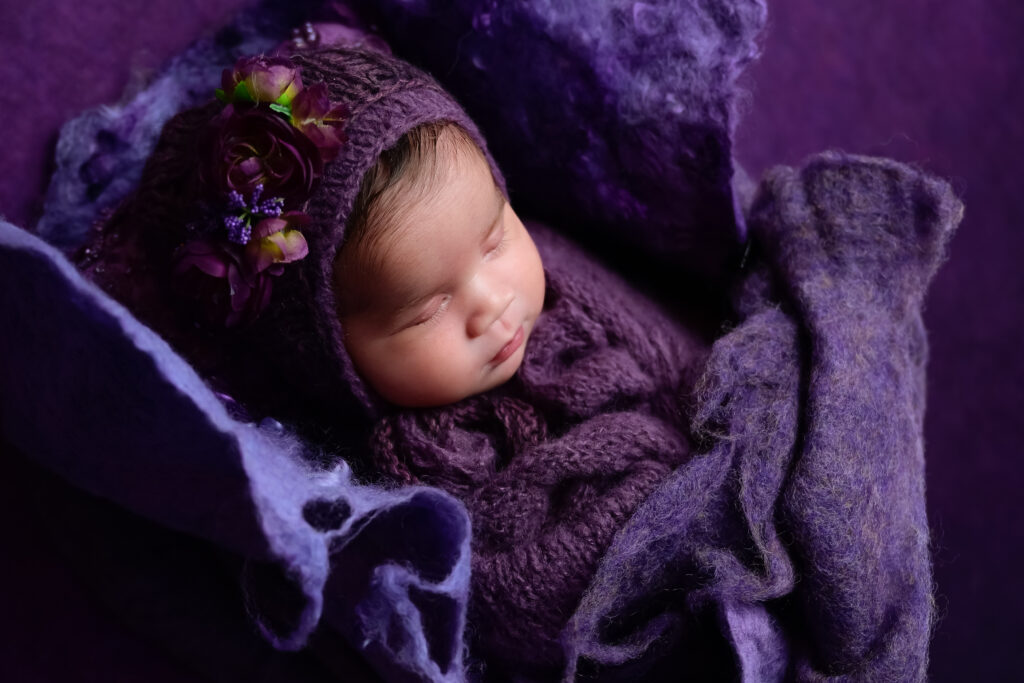 Newborn photo session with baby girl sleeping in multiple layers of various shades of deep purple.