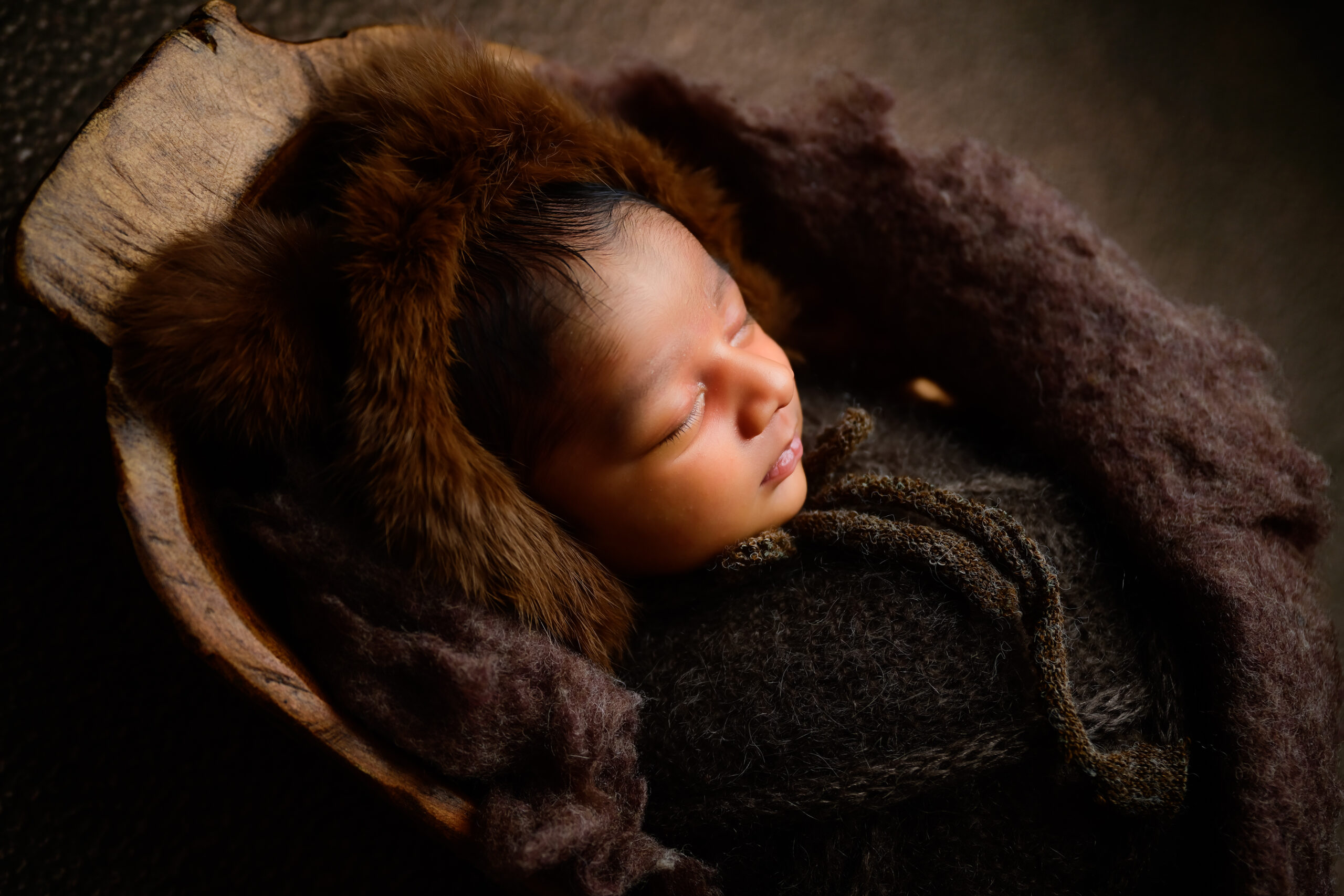 Newborn wrapped in dark browns and fluff posed in a dough bowl for newborn photography session.