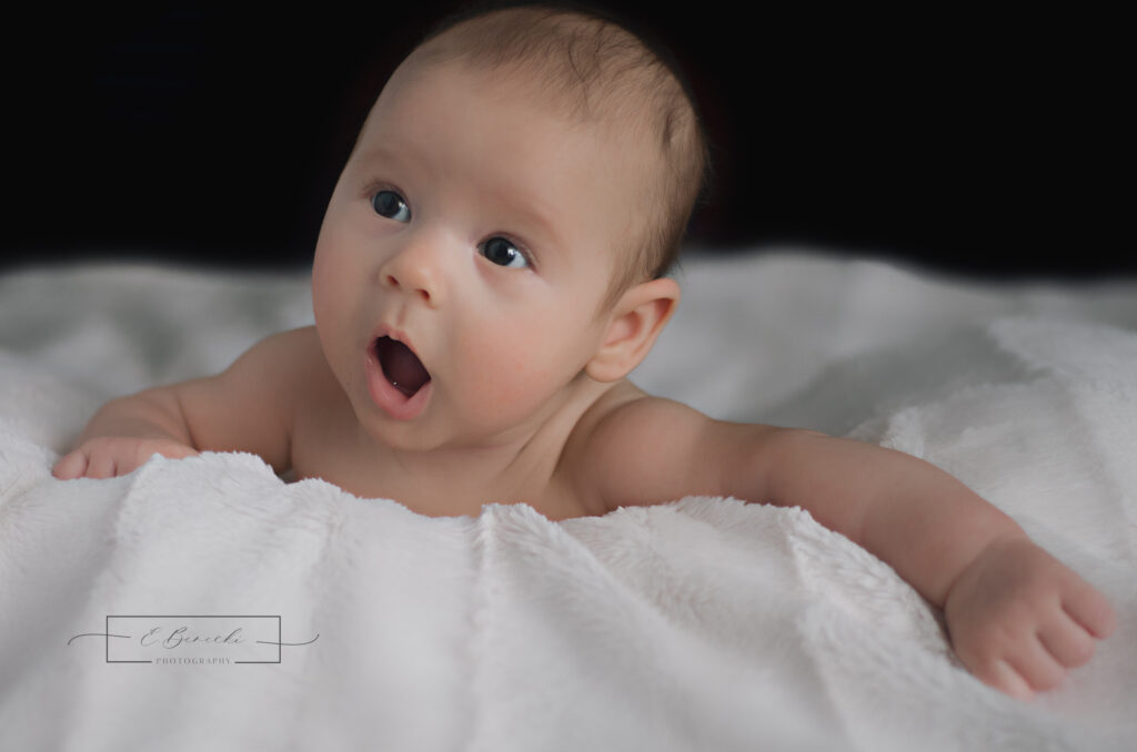 Infant photographed during tummy time on a soft white blanket. Image by E. Benecki Photography.